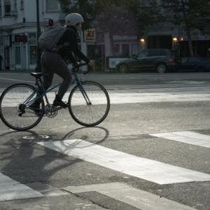 A bicyclist with a backpack and helmet is seen in the street adjacent to a crosswalk. 