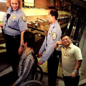 A man smiles in front of a picture of a three people with one of them in a wheelchair in front of an elevator.