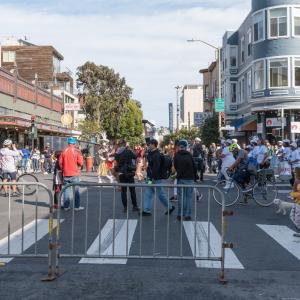 A large crowd of people at a street fair with blockades at the crosswalk.