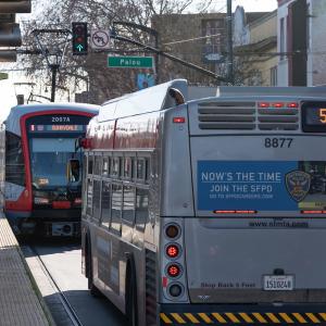 A bus and light rail vehicle at a stoplight near a transit platform during the day 