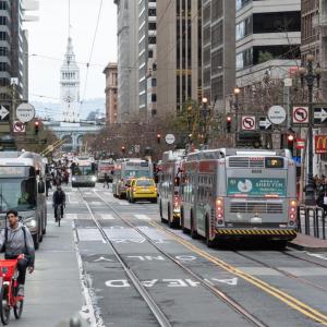 A view down Market Street toward the Ferry Building with taxis, buses and people bicycling and walking