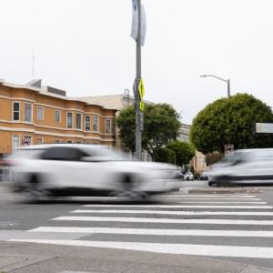 A white car appears blurry as it speeds through an intersection.
