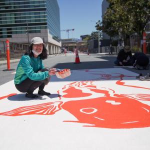 Photo of a community member painting a street mural on a SoMa Slow Street. Photo credit: Erina Alejo