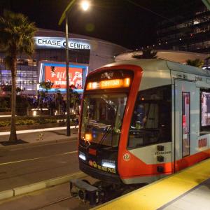 A light rail train stopped at a platform in front of the Chase Center arena in San Francisco.