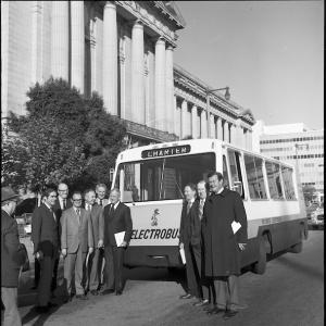 A black and white photo of an early stage Electrobus with a group of people posing for a photo.