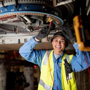 Jeena Villamor makes a repair for the SFMTA. She wears a yellow safety vest and works on overhead equipment. 