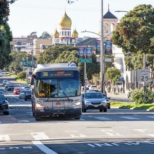A 38 Geary bus heads east on Geary Boulevard, passing 21st Ave. in a designated transit lane. Cars follow in adjacent lanes.