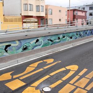 We see artwork on a new L Taraval accessible boarding platform with a freshly paved road beside it and the word "slow."