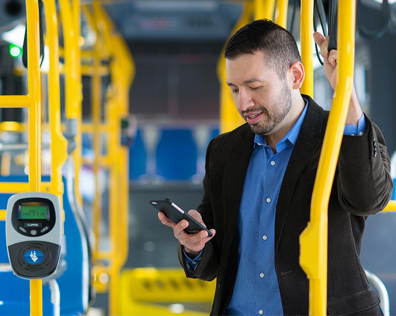 man on bus using smartphone near clipper card reader