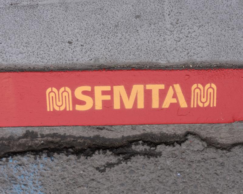 closeup of red color curb with letters SFMTA and new M logo