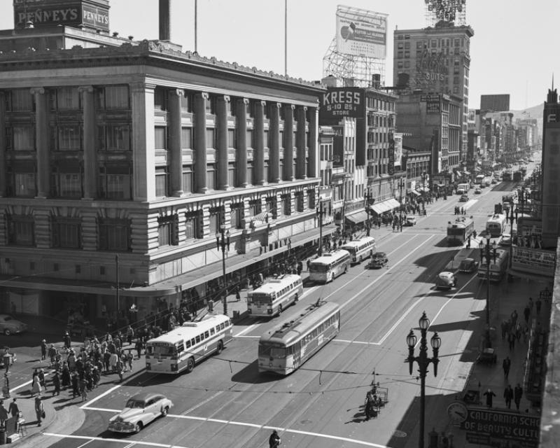 Black and white photo showing a view from above looking west/south west on Market Street from Eddy Street showing buses, streetcars, and pedestrians traveling on the street. Taken in July 1947.