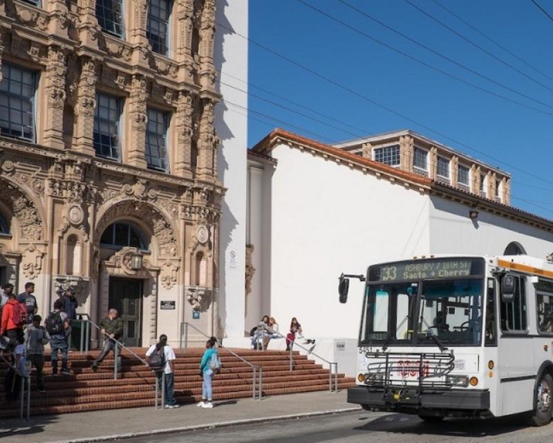image of White and orange Muni trolley bus sits in front of Mission High School while students mingle