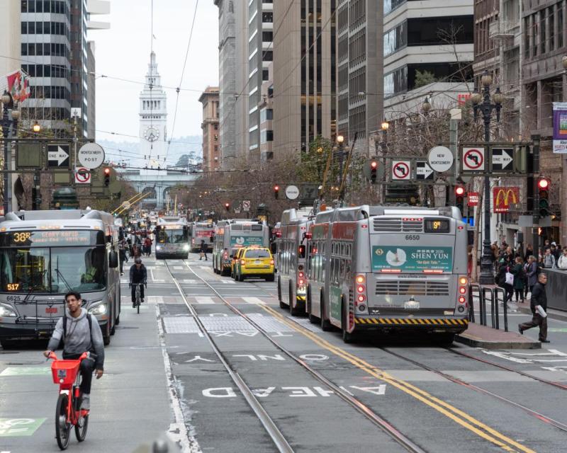 A view down Market Street toward the Ferry Building with taxis, buses and people bicycling and walking
